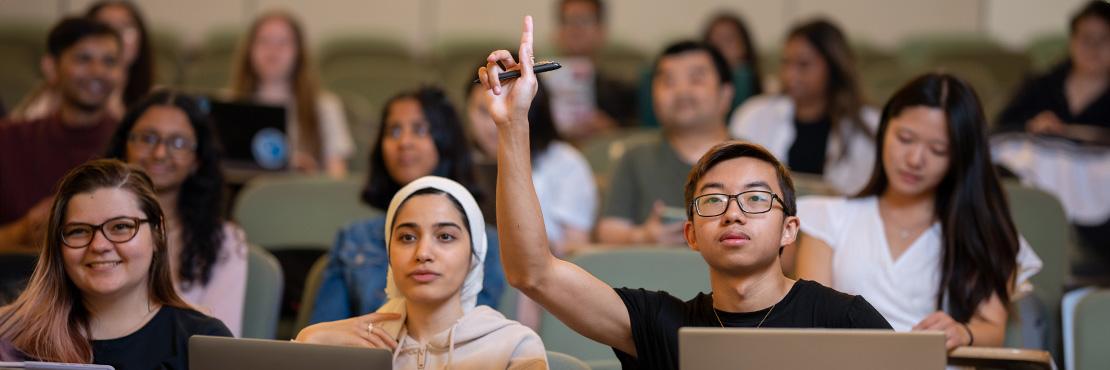 students sitting in lecture hall, with one student with their hand up