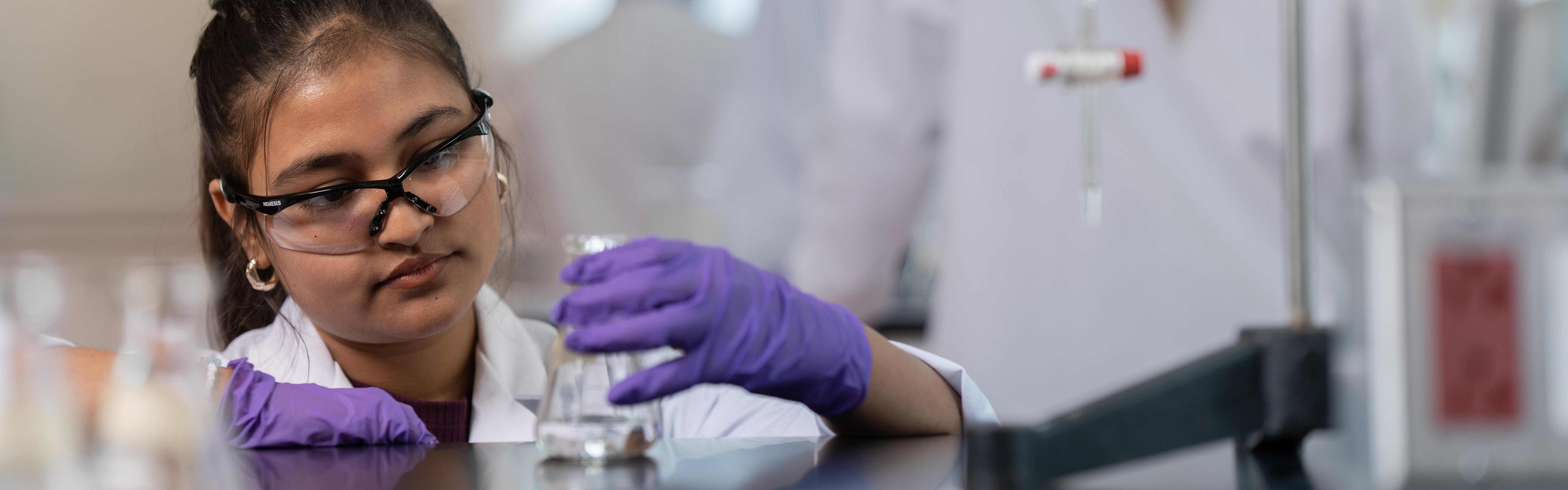 A female student with a purple lab glove on examining a beaker
