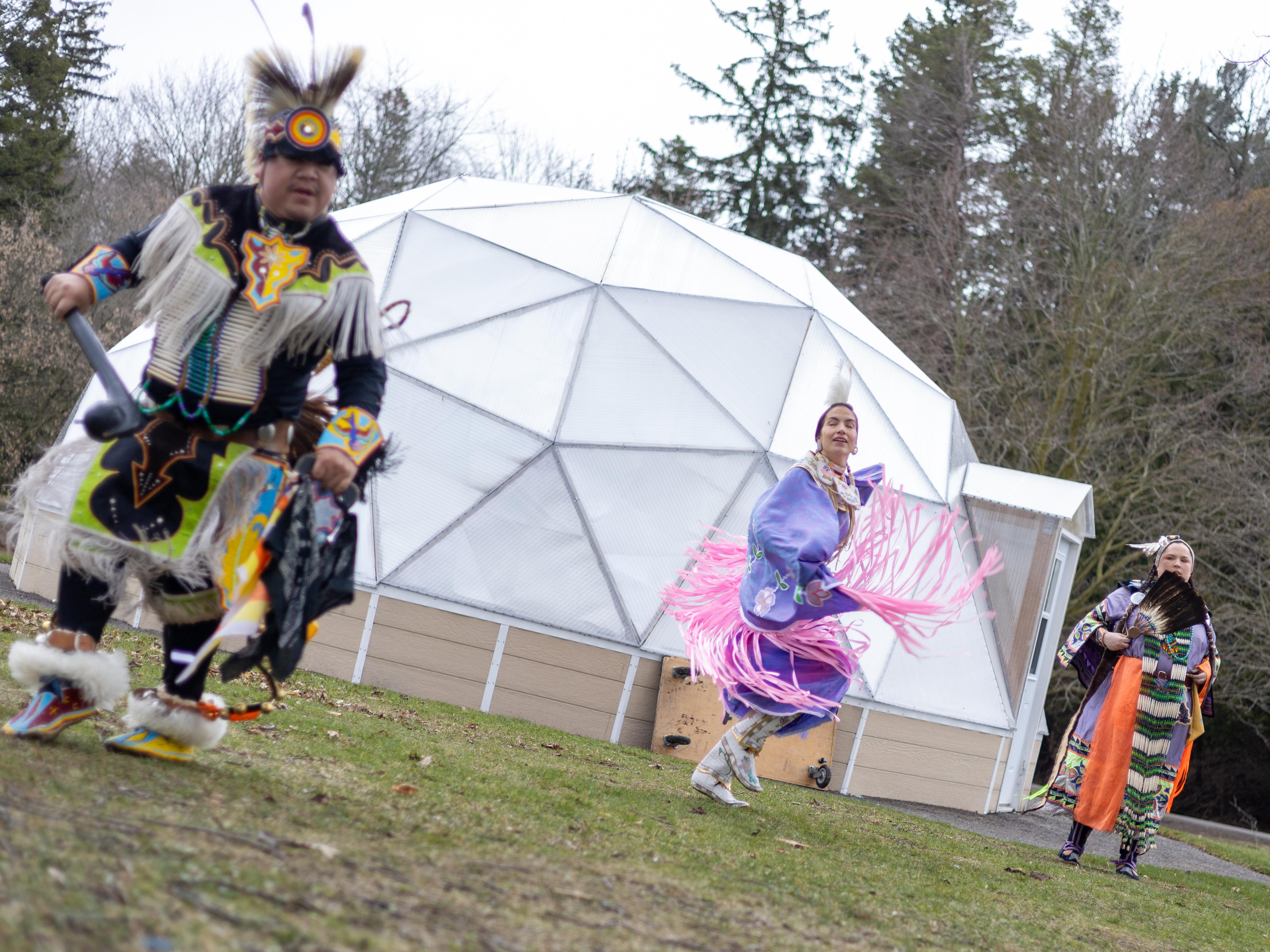 Indigenous performers adorned in bright ornate attire dance outside of a geodesic greenhouse located near the University of Toronto Scarborough.