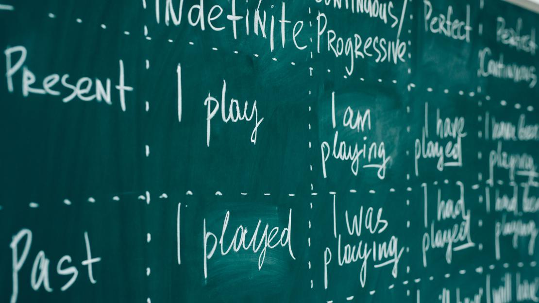A photo of a chalkboard with verb tenses written on it
