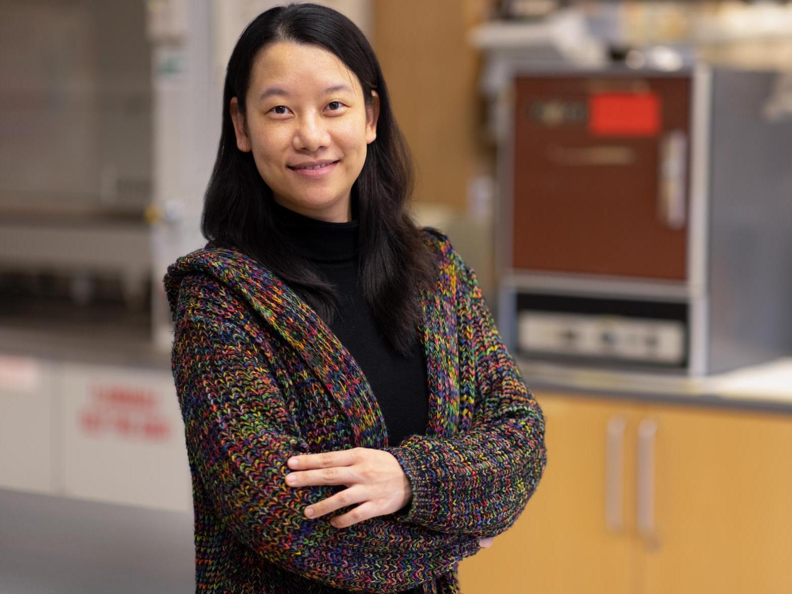Professor Xue Pan standing arms crossed in sweater in a lab