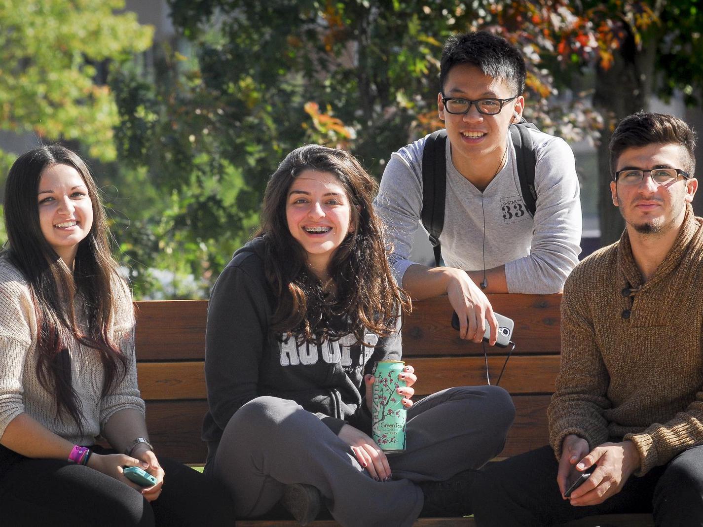 Four students sitting on a bench out side of MW building.
