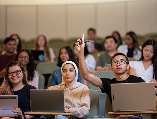 students sitting in lecture hall, with one student with their hand up