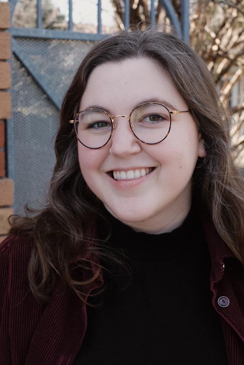 Headshot of Katie Mackinnon wearing gold and brown framed glasses with a black turtle neck shirt.