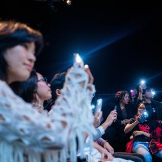 Student audience waving their cellphone flashlights at the concert