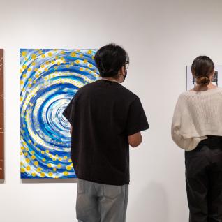 Two students viewing two different artworks on the gallery wall.