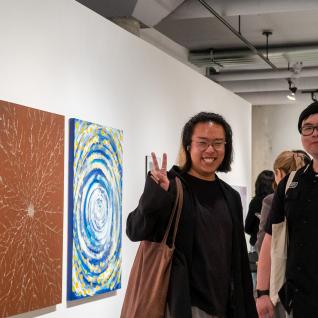 Two students taking photos together beside a painting series.