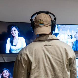 A viewer listening to a video project with headphones standing in front of two sets of TV screens side by side.