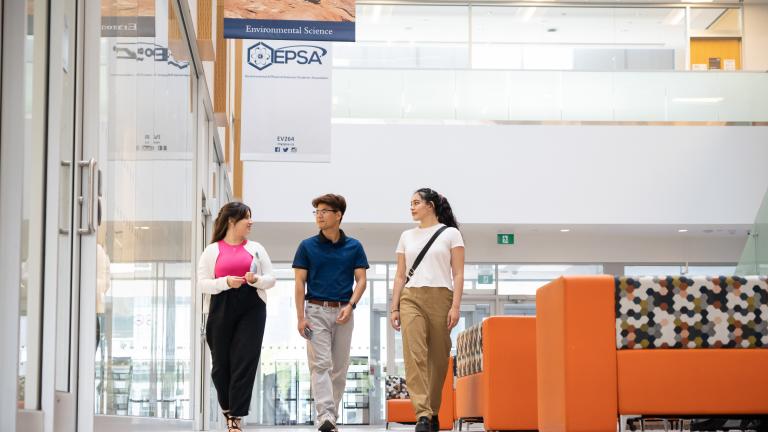 Three students walking through a lobby with bright orange furniture