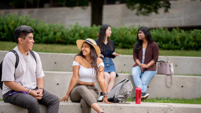 Students outside sitting on large cement steps, in discussion, two in the foreground and two in the background