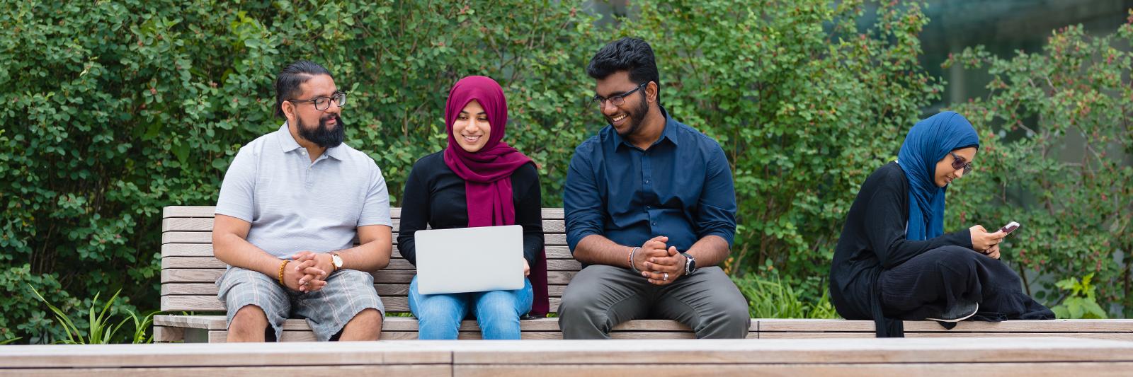 students sitting on bench looking at a laptop