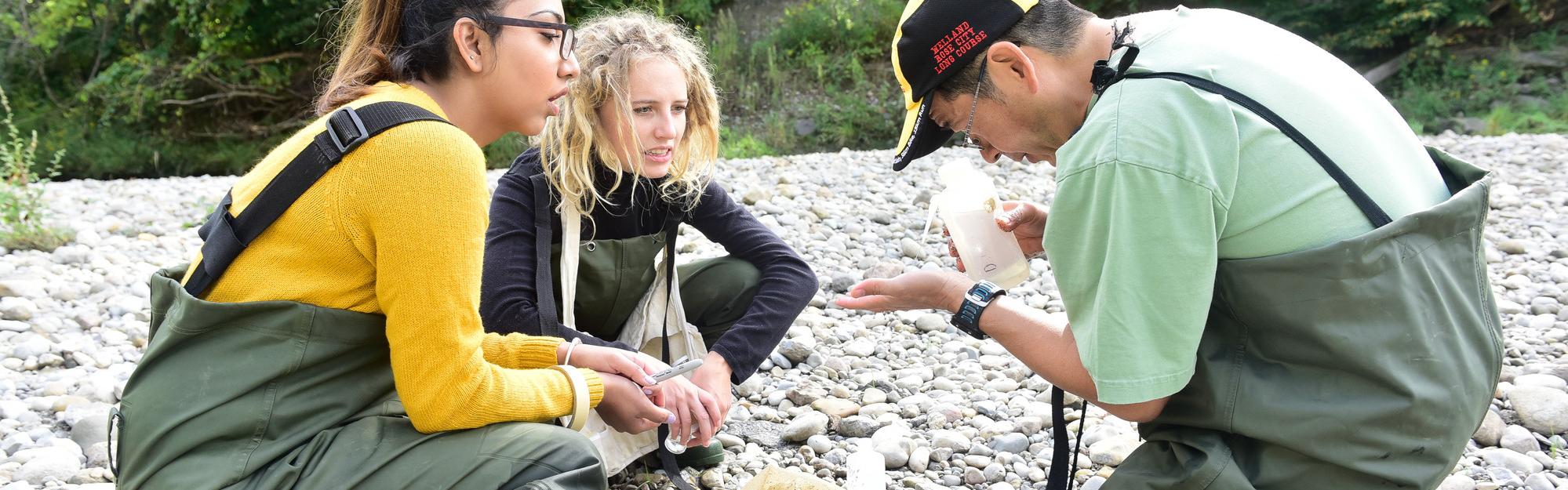 Students on field trip, on rocks by a creek, examining a sample