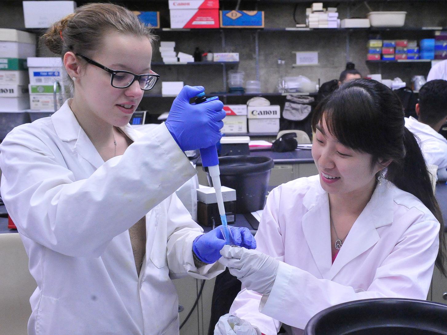 Two female students in a lab with a dropper and a slide