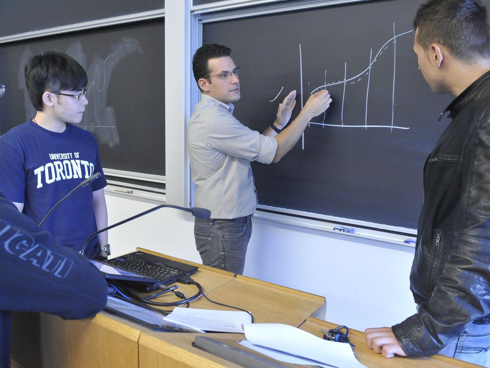 A professor showing a curve on a blackboard with three students looking on