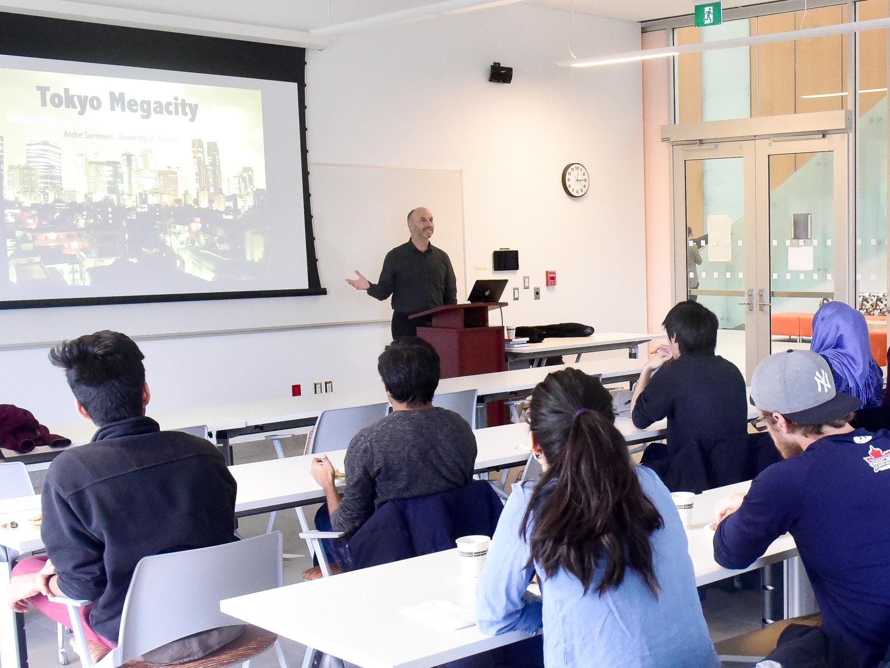 A professor in front of a slide that says Tokyo Megacity, with students listening in the foreground in a classroom setting