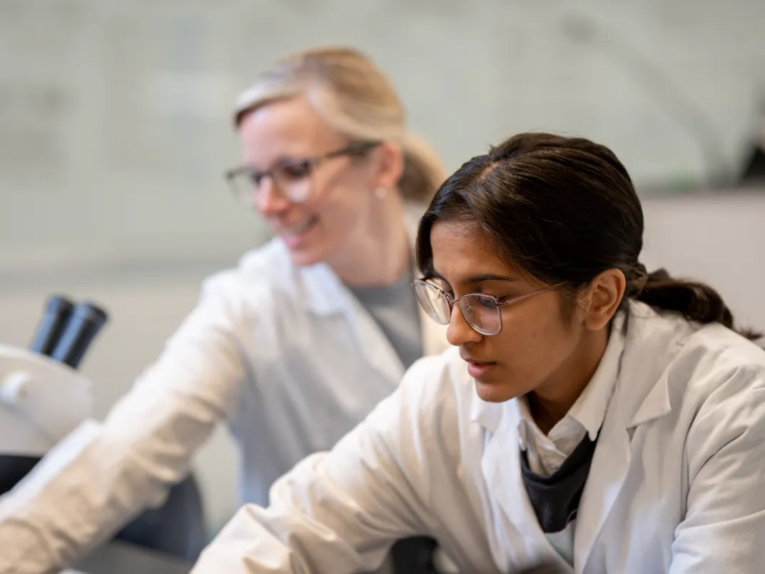 Two women in lab coats reaching forward