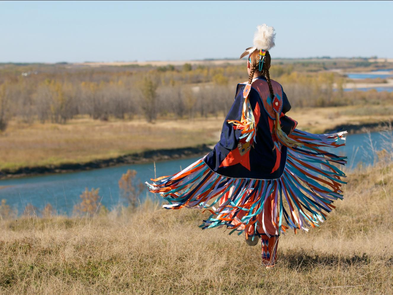 A woman in traditional first nations clothing looking out over a valley