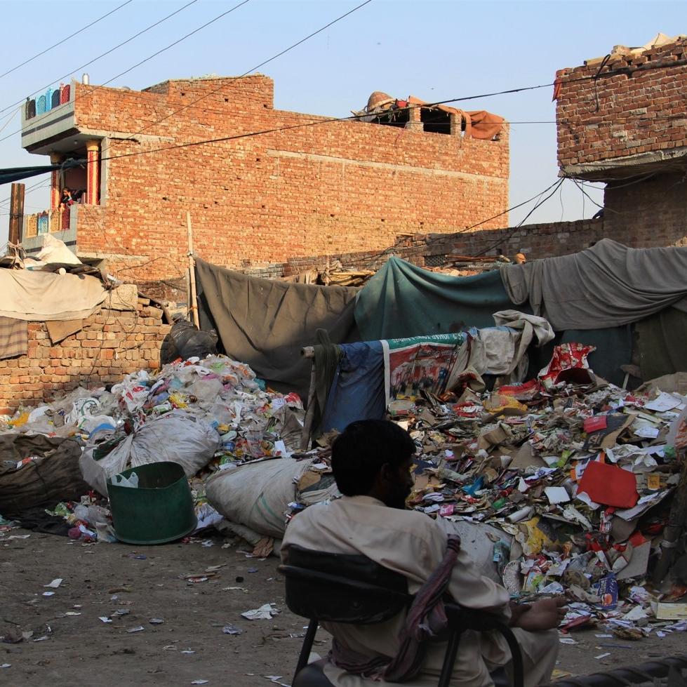 A waste worker in Pakistan sits in a chair beside a pile of refuse