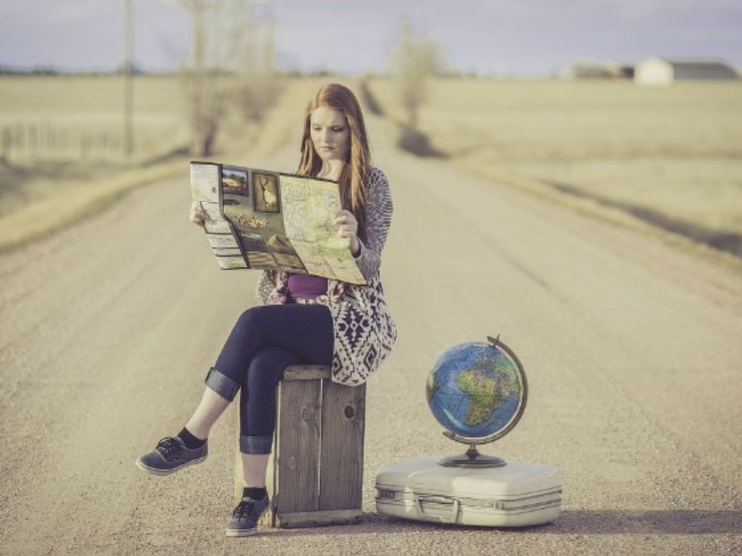 Woman sits on a suitcase reading a map