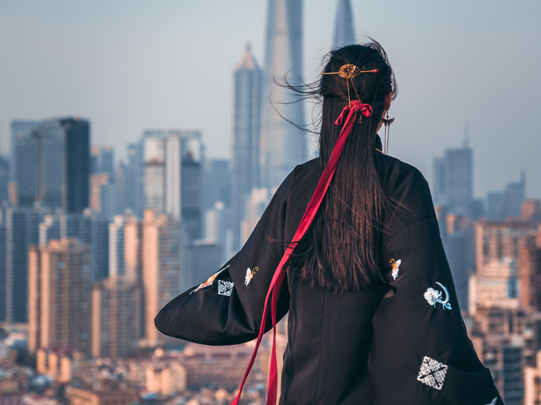 Girl with long hair ribbon faces a cityscape