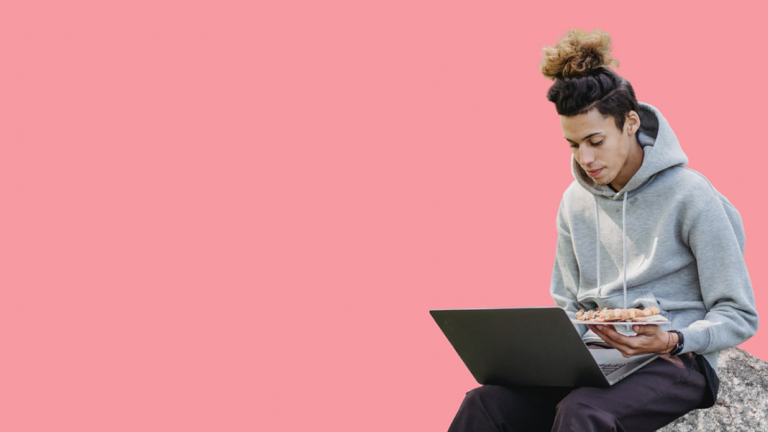 person sitting on a rock on a laptop with pink background