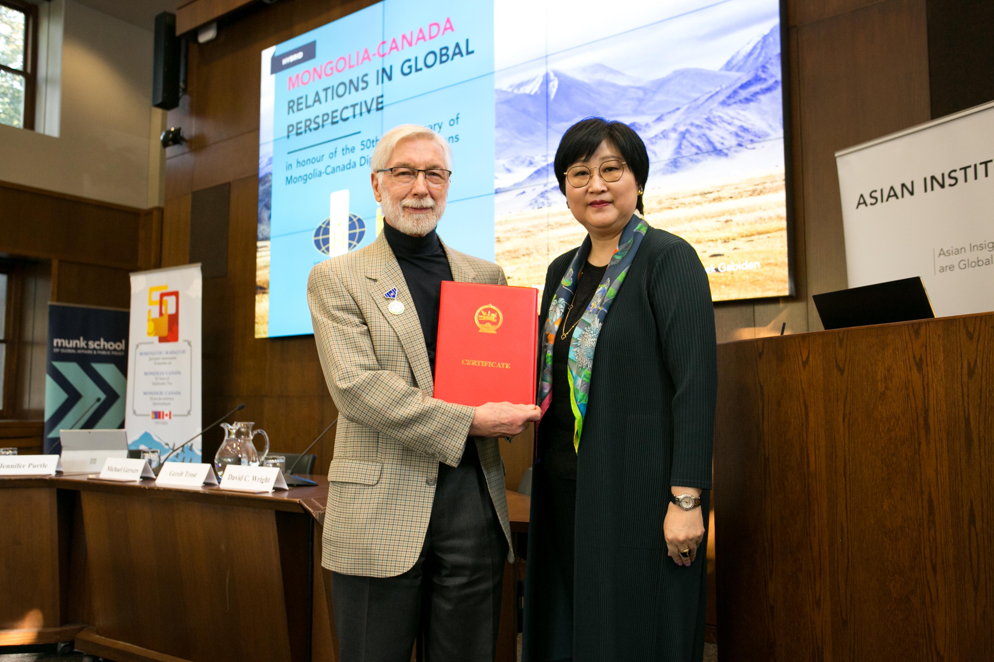 Professor Michael Gervers posing for a photo with Mongolian Ambassador Madam Sarantogos Erdenetsogt while holding the certificate for the Medal of Friendship 