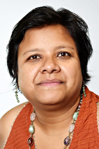 Headshot of Jayeeta Sharma wearing an orange sleeveless shirt, green beaded earrings and a necklace with amber, rose and mint green coloured stones
