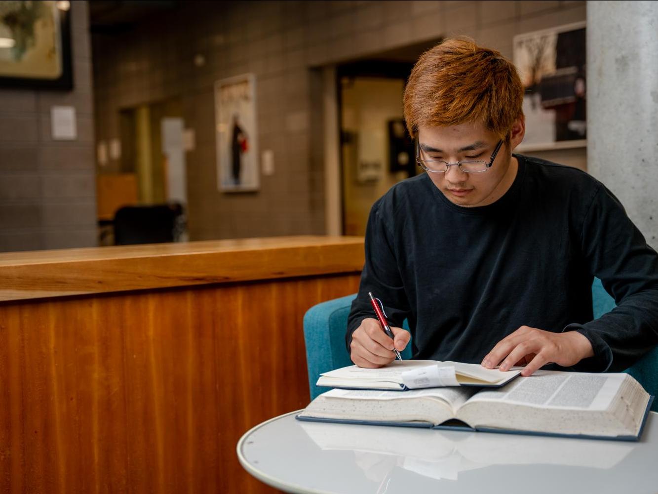 Student in the UTSC Library, writing in a notepad.