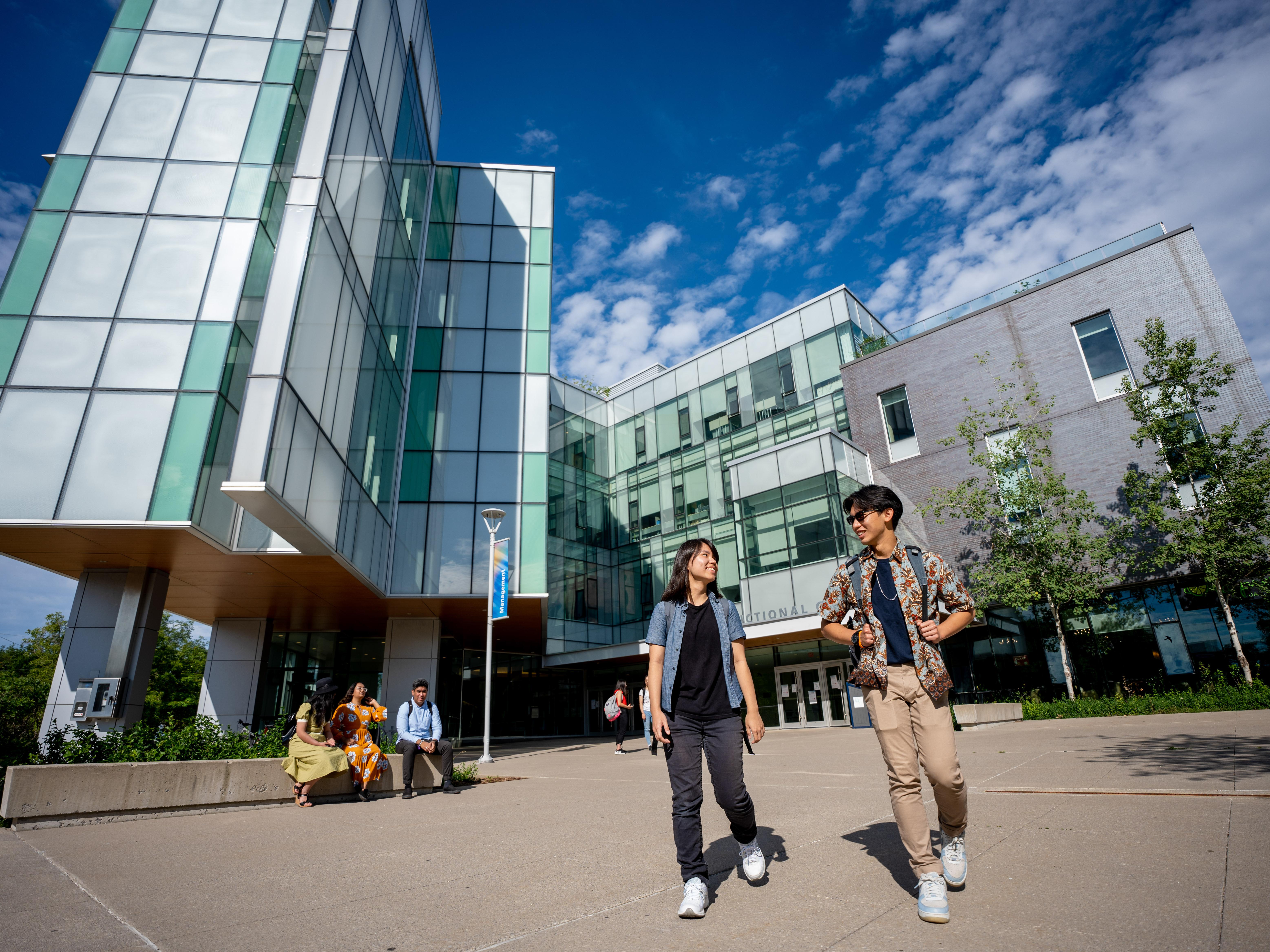 Students walking outside the Instructional Centre, in summer clothing.