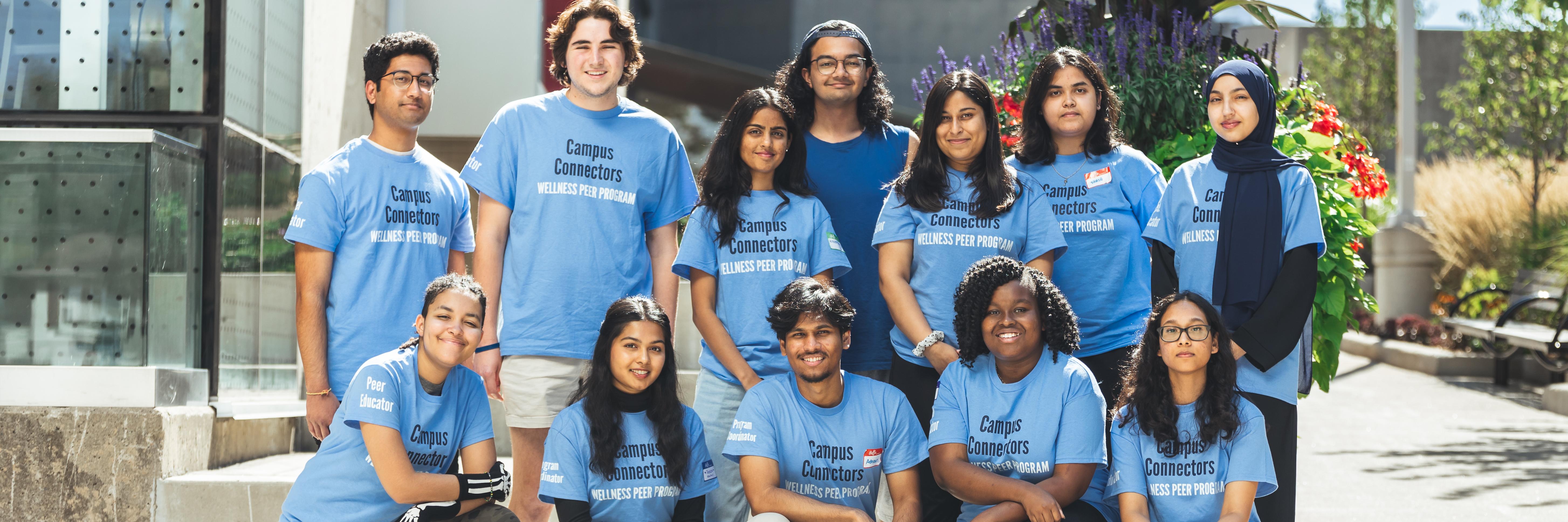 Group of 12 students in the Campus Connectors Team wearing uniform Wellness Peer Program shirts