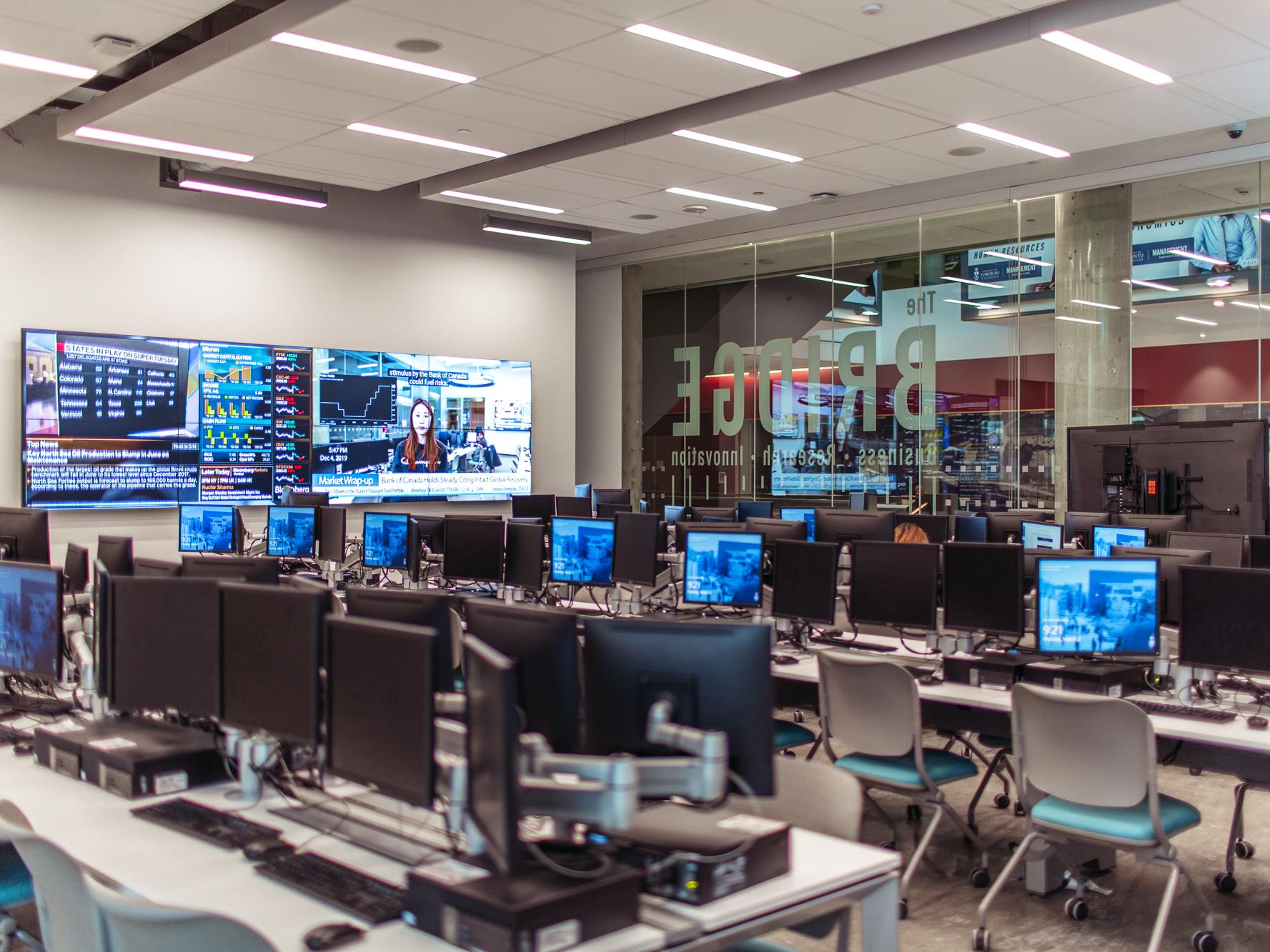 A glass-walled classroom with dozens of screens resembling a trading floor.
