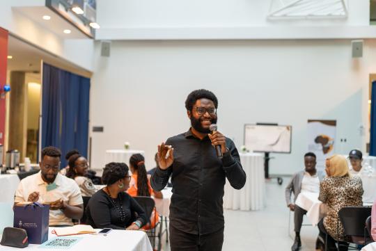 Efosa Obano smiles widely while speaking into a microphone in the Instructional Centre atrium at the University of Toronto Scarborough during an investor mixer event attended by startup founders from the African continent.