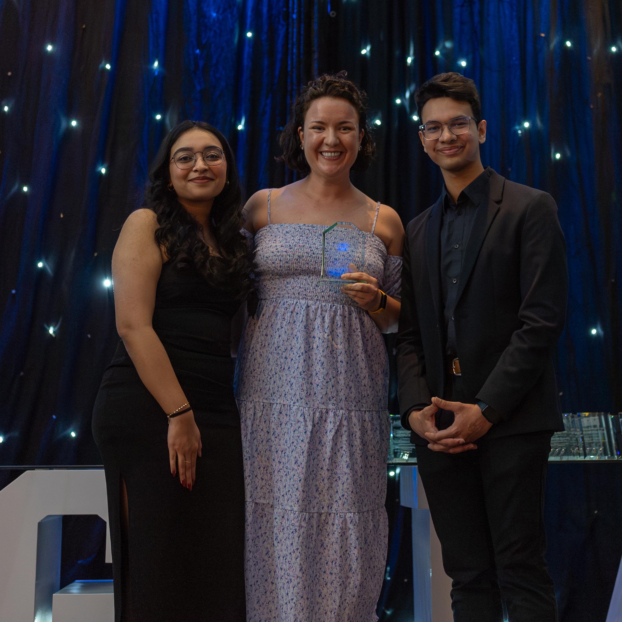 Maria Shibaeva-Escarraga smiles widely while being presented the Professor of the Year Award by two formally attired students during the U of T Scarborough Management Gala