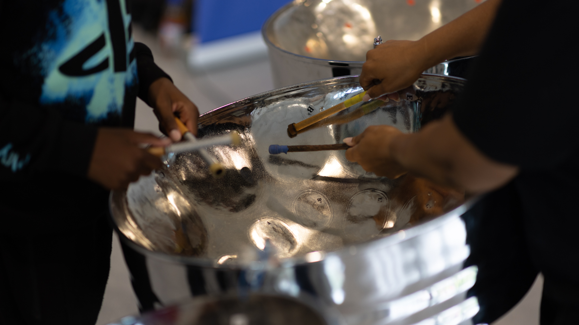 Hands playing a steel pan instrument.
