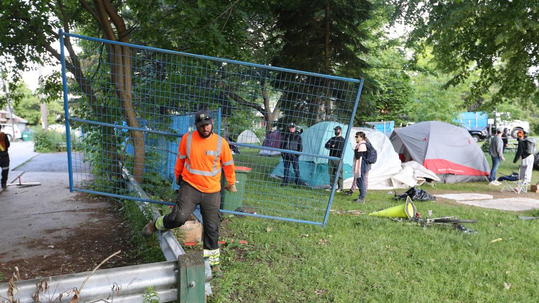 Security workers set up fence around a homeless encampment