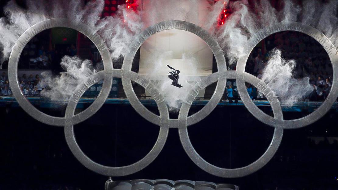 A snowboarder flies through the Olympic rings