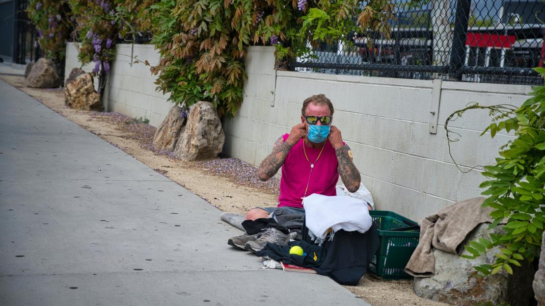 A man sitting on the ground puts on a face mask.