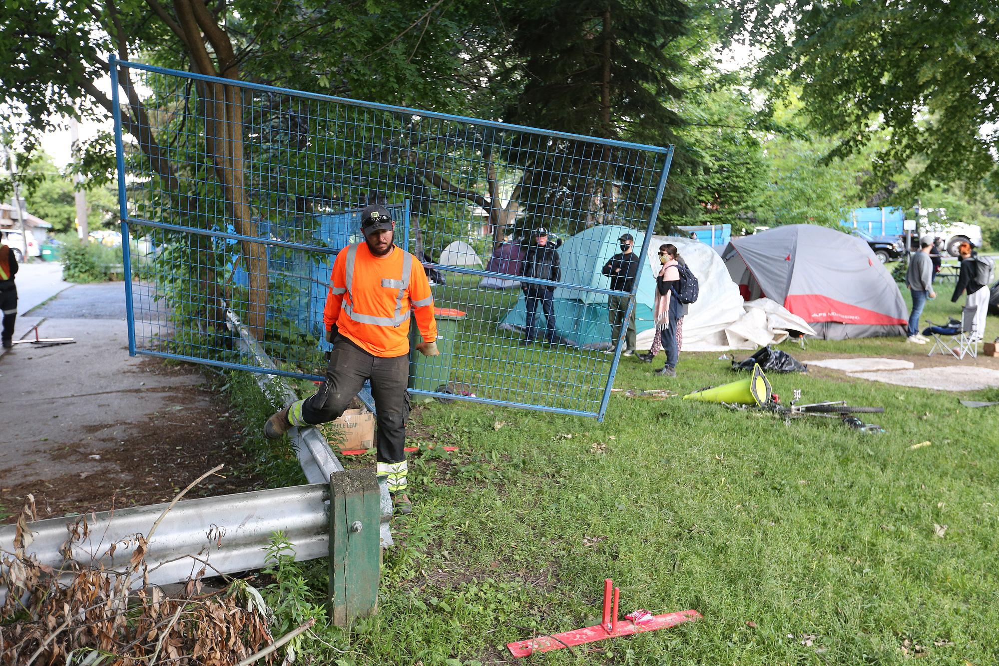 Security workers set up fence around a homeless encampment