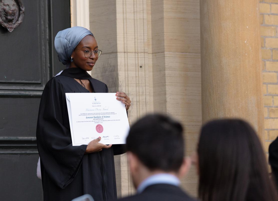 U of T Scarborough grad holding diploma outside of convocation hall