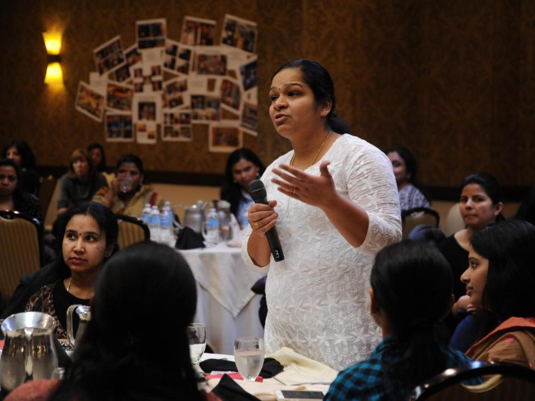 A woman speaks with a microphone at an event intended to bring community voices into surveys