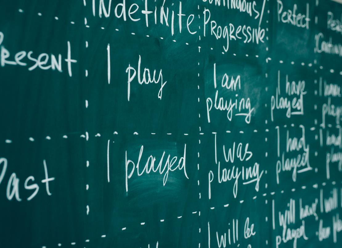 A photo of a chalkboard with verb tenses written on it