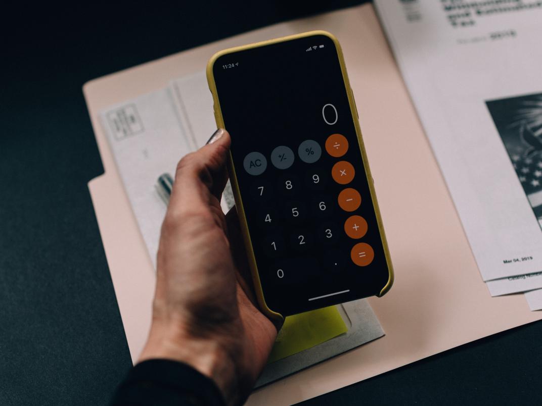 A hand holds a calculator over a folder.