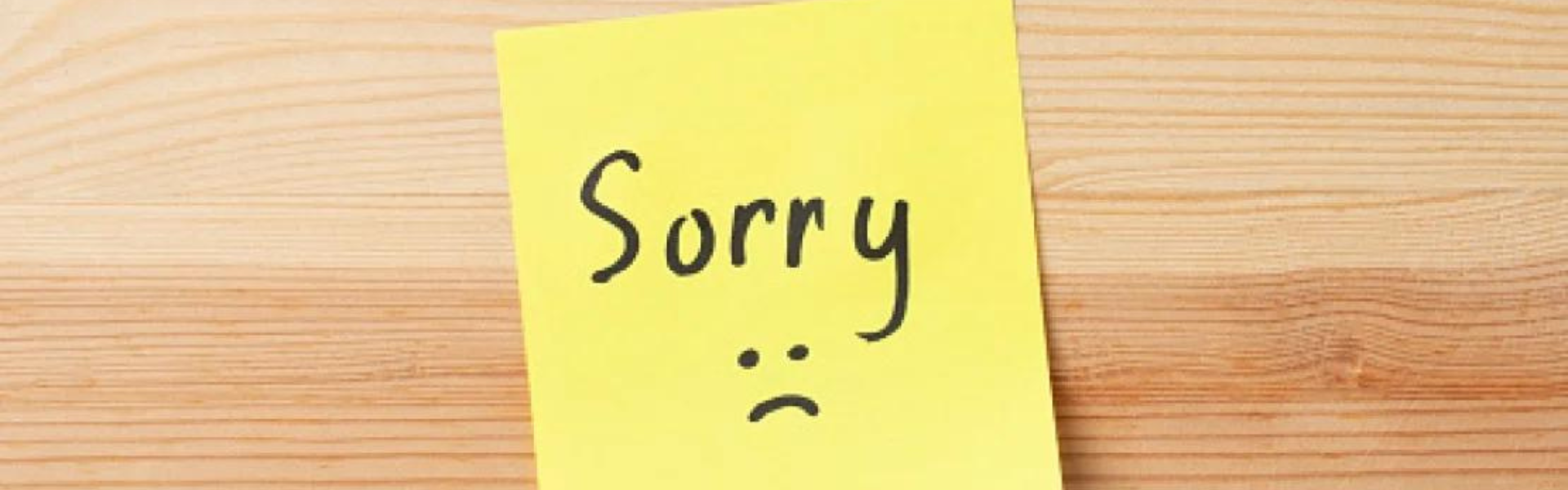 Image of woodgrain with a yellow post-it note saying "Sorry" and a frowning face