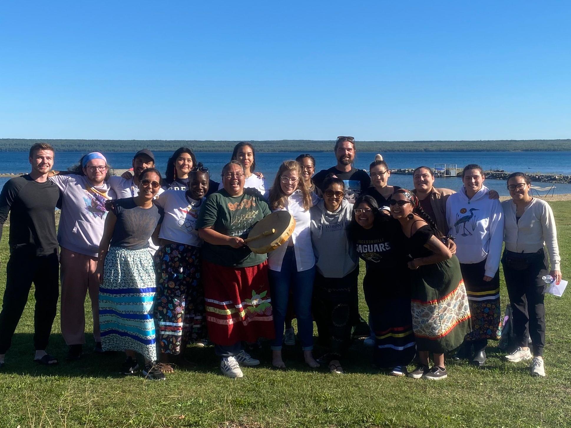 A group of students posing with Danielle Roy, founder of the Odemin Kwe singers beside a lake