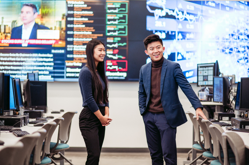Woman and man standing in computer lab with large screens in background