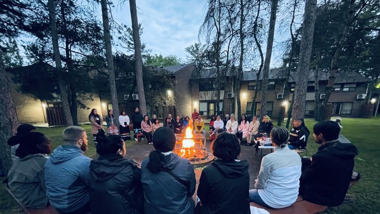Members of Campus Curriculum Working Circle sitting around bonfire at sunrise outside of student residences