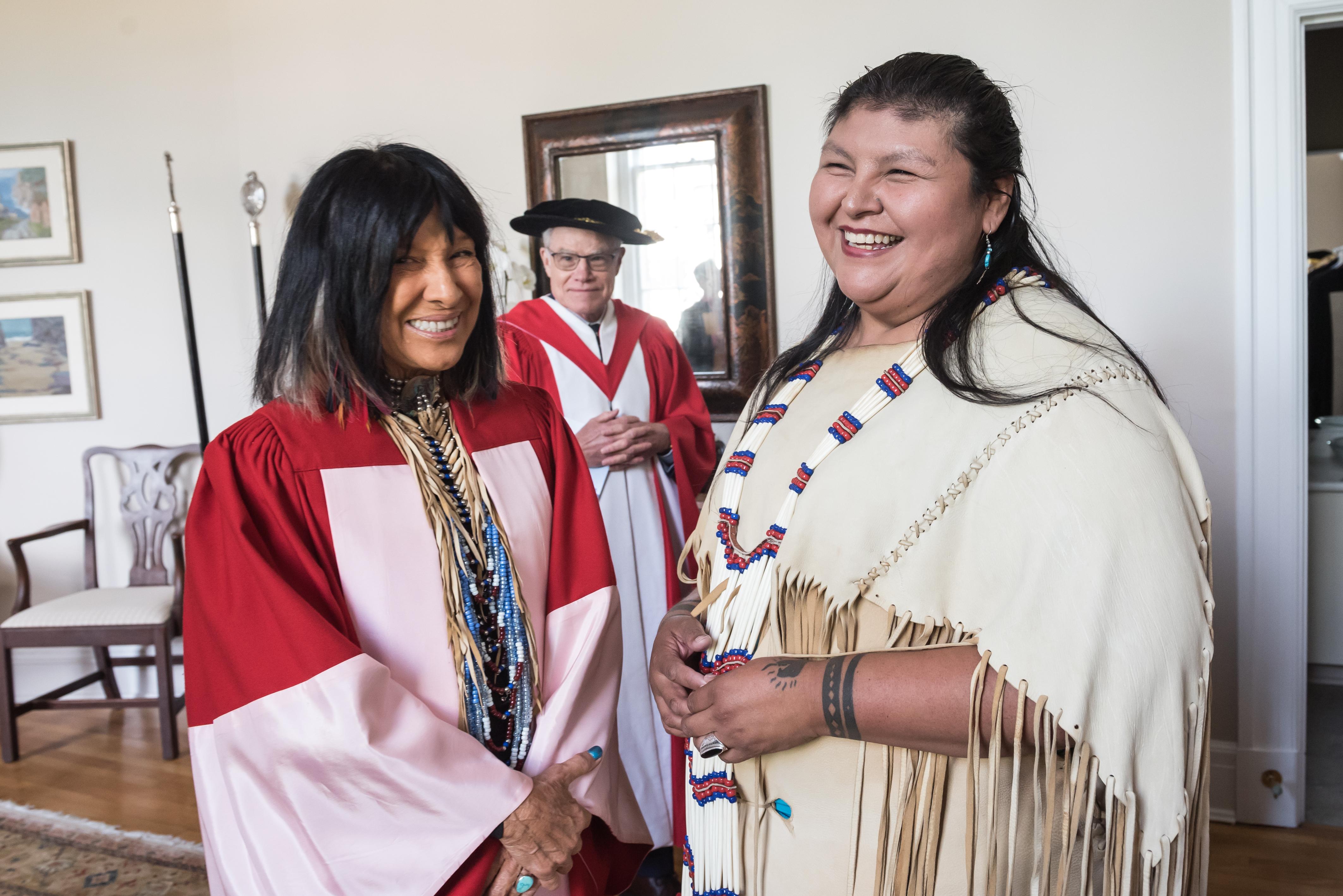 Elder Wendy Phillips smiling with honorary graduate Buffy Sainte Marie, with Vice-President & Principal Bruce Kidd in background