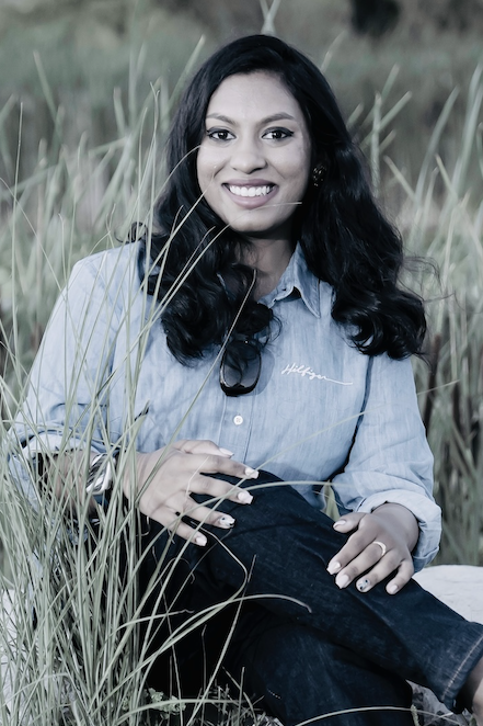 Sayilaja sitting on a rock in a field, smiling.